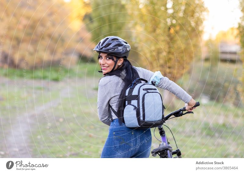 Positive Frau mit Fahrrad in herbstlicher Landschaft Herbst Wald aktiv Glück Natur Mitfahrgelegenheit Rucksack Schutzhelm heiter Lächeln Nachlauf Weg Aktivität