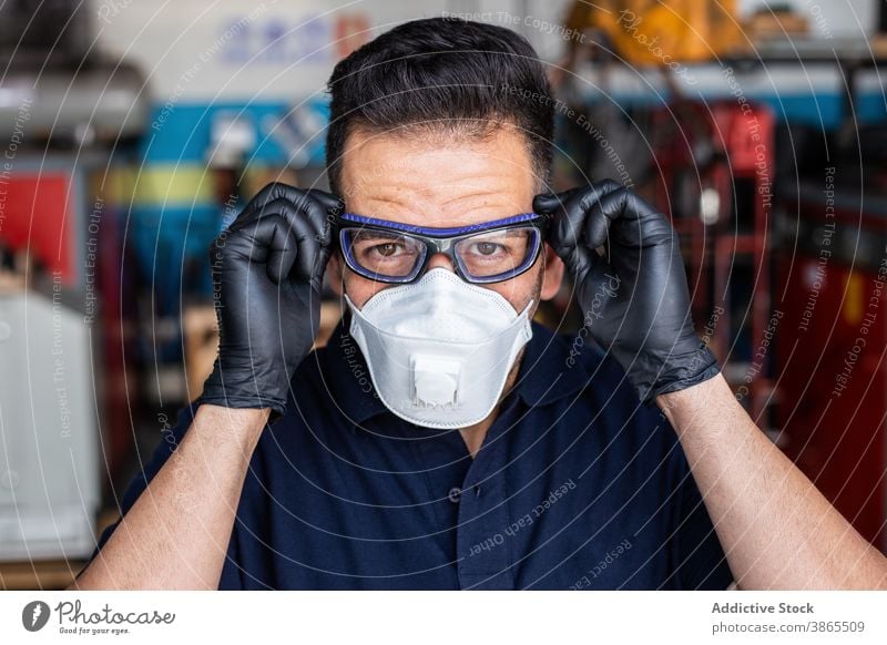 Männlicher Techniker setzt Schutzbrille auf Mann Mechaniker angezogen Garage Atemschutzgerät Handschuh vorbereiten behüten Arbeiter männlich Latex Erwachsener