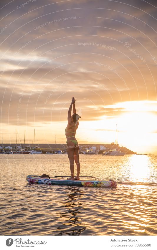 Schlanke Frau übt Yoga auf Paddelbrett bei Sonnenuntergang Holzplatte Berge u. Gebirge urdhva hastasana Pose Asana Silhouette MEER Wasser Schwimmer schlank
