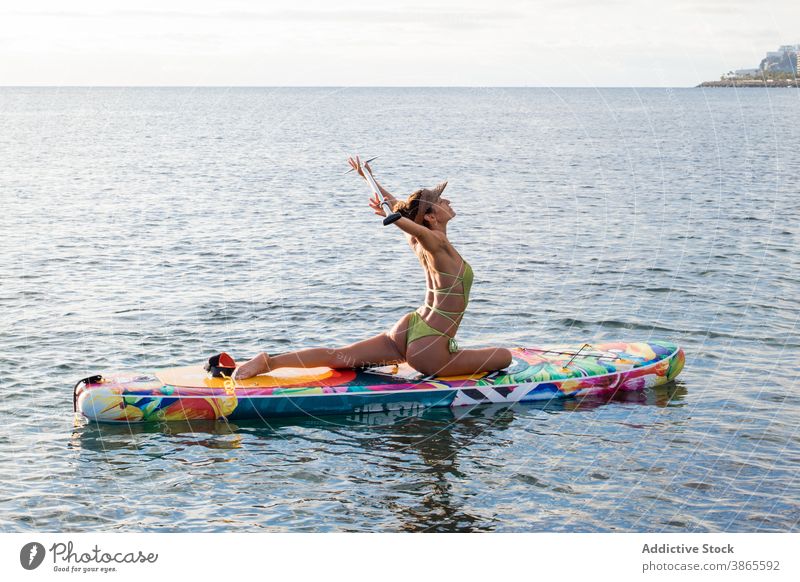 Schlanke Frau macht sitzende Yoga-Pose auf Paddle Board Paddel Holzplatte Halbtaube Asana MEER Wasser schlank beweglich passen positionieren Gesundheit
