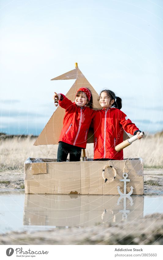 Mädchen spielen in Karton Boot in Pfütze Schachtel Kind Zusammensein Spaß haben Vorstellungskraft Spiel Fernglas handgefertigt heiter Glück genießen Lächeln