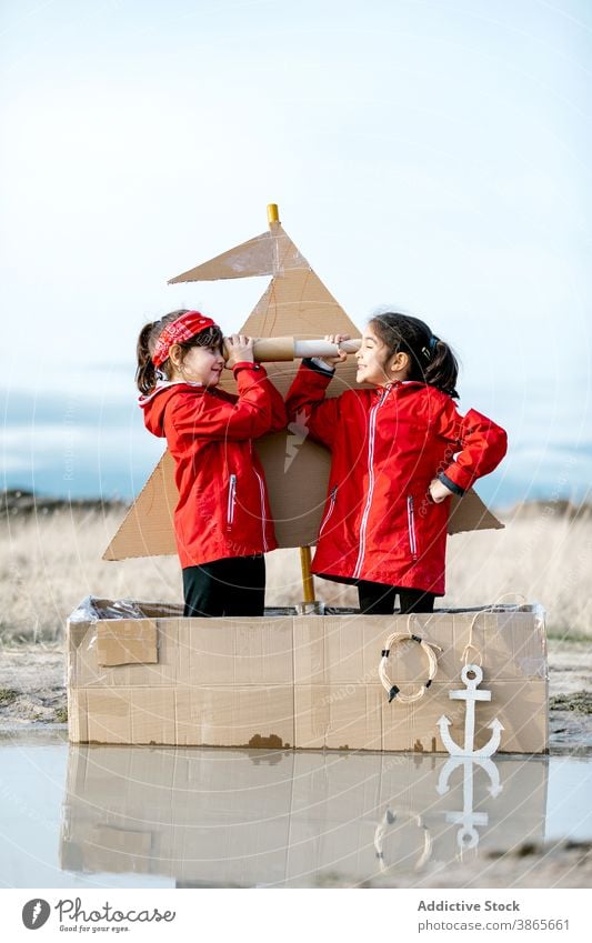Mädchen spielen in Karton Boot in Pfütze Schachtel Kind Zusammensein Spaß haben Vorstellungskraft Spiel Fernglas handgefertigt heiter Glück genießen Lächeln
