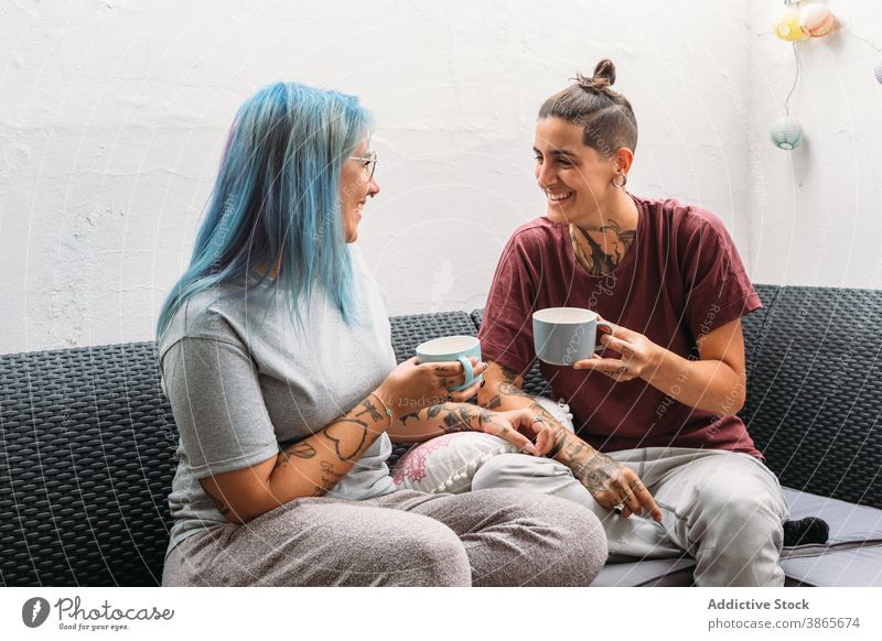 Glückliche Freundinnen genießen heiße Getränke auf dem Sofa Frauen trinken Lächeln ruhen Paar lesbisch Becher heimwärts gemütlich informell auflehnen alternativ