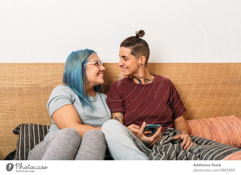 Glückliches lesbisches Paar mit Smartphone Frauen benutzend Bett Lächeln heimwärts Zusammensein gemütlich Freundin Apparatur Gerät ruhen soziale Netzwerke