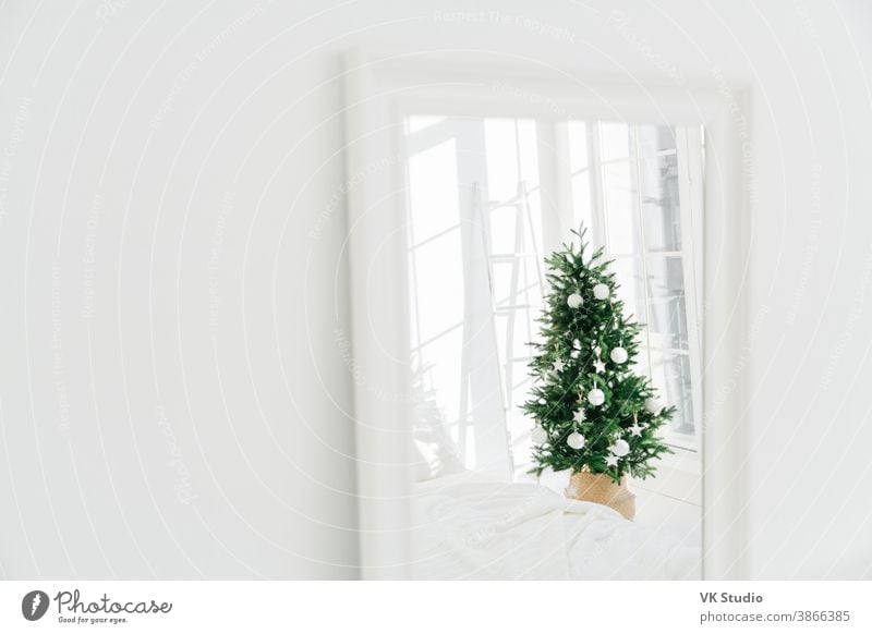 Geschmückter Weihnachtsbaum im Spiegel reflektierend, weißer geräumiger Raum. Schlafzimmer mit Neujahrsdekoration. Moderner klassischer Stil. Heiligabend zu Hause