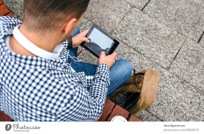 Nicht erkennbarer junger Mann mit Tablette unkenntlich Draufsicht benutzend soziales Netzwerk im Freien Kopfhörer Rucksack Typ Internet männlich