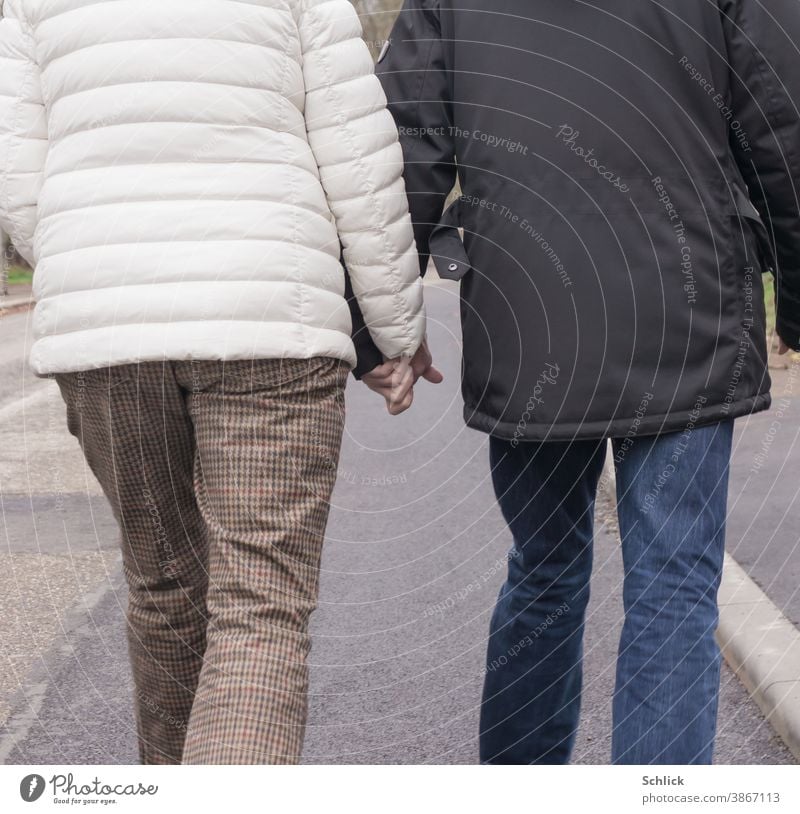 Liebe älteres Paar in Winterkleidung halten Händchen und gehen auf der Straße Rückansicht Liebespaar Händchenhalten Senioren Asphalt Jacken blau weiß Mann Frau