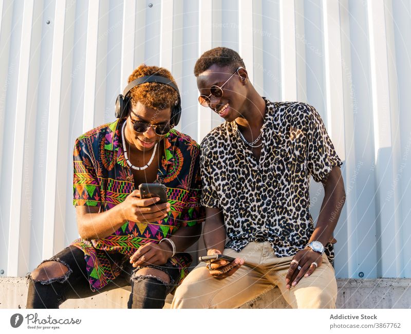 Positive junge Männer, die gemeinsam das Handy in der Stadt betrachten Freund Stil tausendjährig Zusammensein Smartphone trendy Mode ethnisch schwarz