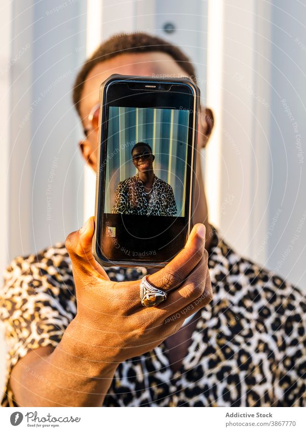 Schwarzer Mann macht Selfie mit Smartphone in der Stadt Großstadt urban Stil Outfit gutaussehend Lächeln fotografieren männlich ethnisch Afroamerikaner schwarz