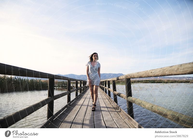 Frau im Kleid geht auf hölzerner Promenade Steg See Spaziergang Sommer selbstbewusst Weg jung lässig Lifestyle Urlaub Natur Feiertag Dame Freiheit Erholung