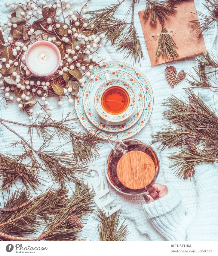 Winter und Weihnachten Lebensstil. Frau hält Teekanne auf weißer Strickdecke mit Tasse Tee, Weihnachtskranz und Tannenzapfen und -zweigen in der Hand. Ansicht von oben