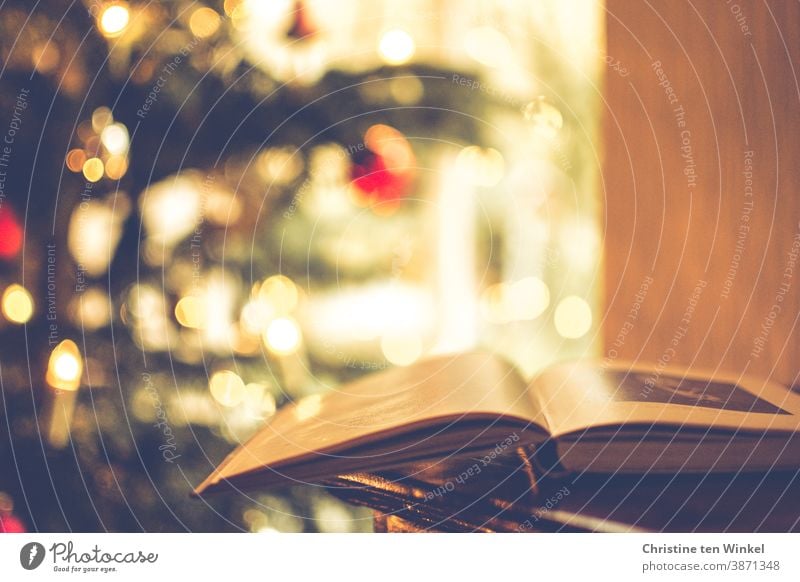 Weihnachtslektüre ...  Ein aufgeschlagenes Buch liegt auf einer Kommode, im Hintergrund sieht man im Gegenlicht unscharf den geschmückten Weihnachtsbaum und ein Fenster