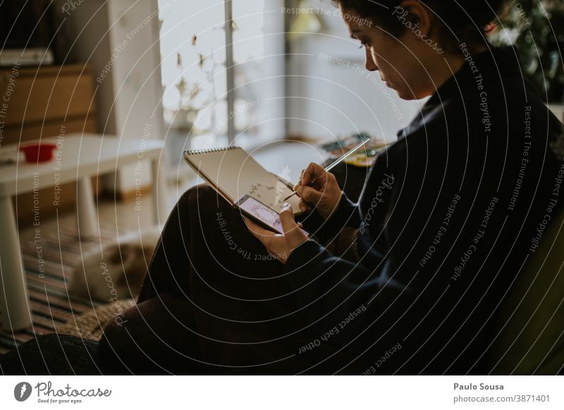 Frau skizziert und benutzt Smartphone 30-39 Jahre lernen Lernen und Wissen Lifestyle zu Hause authentisch Herbst lässig Kaukasier Farbe krause Haare Tag Genuss