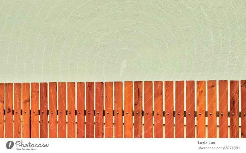 Zaun, braun und orange vor einer Hauswand in hellem Oliv, Vorstadtästhetik Vorgart Wand oliv Fassade Menschenleer Außenaufnahme Farbfoto Mauer Gebäude Tag