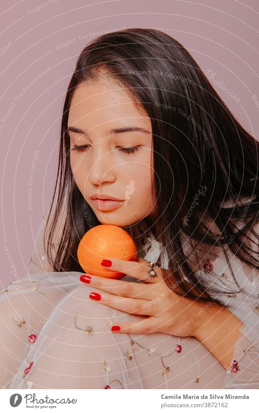 Modell, das eine Orange hält. Studioaufnahme mit rosa Hintergrund. schön Schönheit Pflege Zitrusfrüchte Nahaufnahme Kosmetik Gesicht frisch Frucht Mädchen