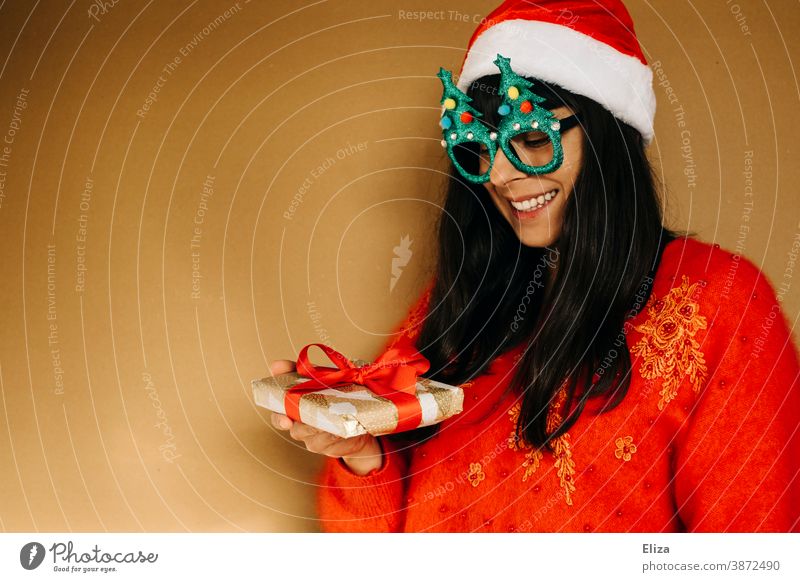 Junge Frau in weihnachtlicher Kleidung blickt lächelnd auf ein Weihnachtsgeschenk Weihnachten Pullover rot Geschenk Bescherung schenken bekommen Freude