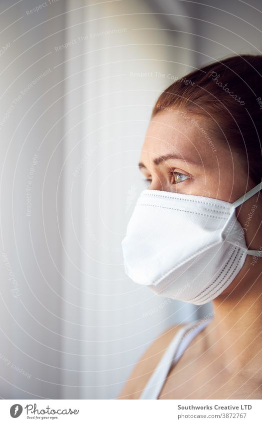 Junge Frau schaut aus dem Fenster und trägt eine Gesichtsschutzmaske. tragend Mundschutz heimwärts behüten Virus Krankheit Krankheiten Grippe Air Gesundheit