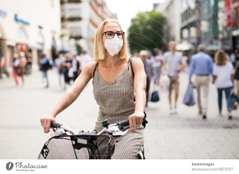 Frau, die auf der Straße in der Stadt Fahrrad fährt und in der Öffentlichkeit eine medizinische Gesichtsmaske trägt, um die Verbreitung des Coronavirus zu verhindern. Neue Normalität während der Covid-Epidemie.