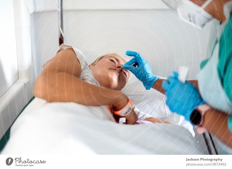 Covid-19-Test bei einer Frau im Krankenhausbett durchgeführt Pandemie COVID19 Prüfung Tupfer professionell Behandlung Prävention blau Handschuhe niederlegen
