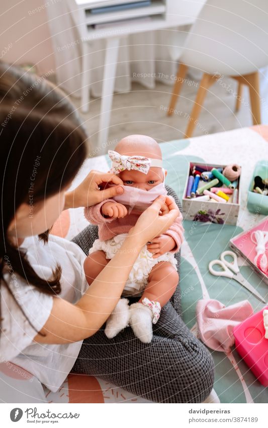 Mädchen probiert ihrer Puppe eine Maske an, die sie gerade näht Einstellmaske Maske aufsetzen Babypuppe Stoffmaske Nähkästchen covid-19 handgemacht Schutz