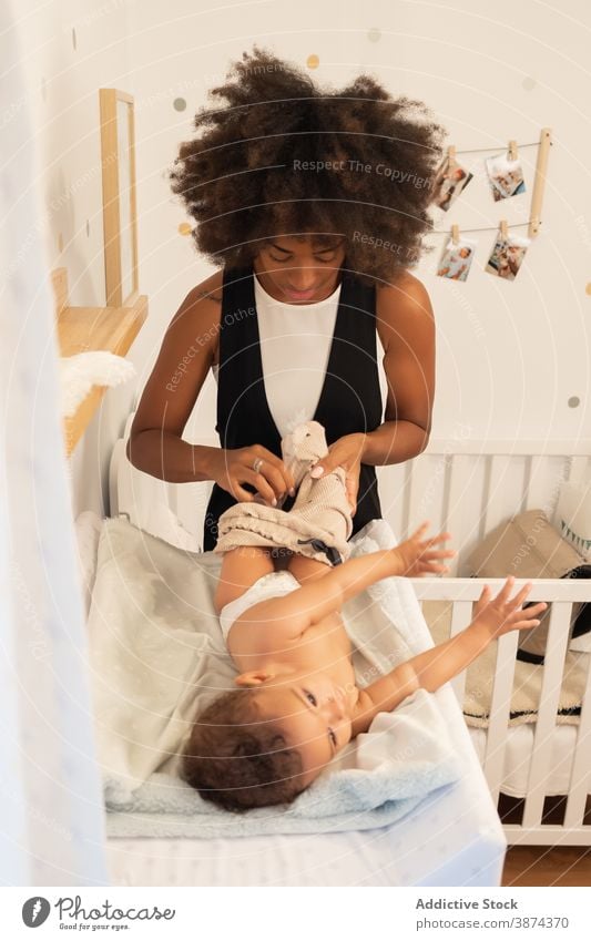 Schwarze Frau setzt auf Kleidung auf Baby Wandel & Veränderung Tisch Mutter angezogen Stoff Hose Pflege Kleinkind wenig ethnisch schwarz Afroamerikaner Lügen