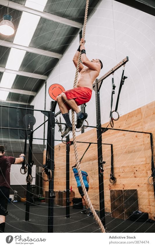 Athletischer Mann klettert Seil im Fitnessstudio Aufstieg Training operativ Sportler stark anstrengen Ausdauer männlich Motivation Aktivität Wohlbefinden