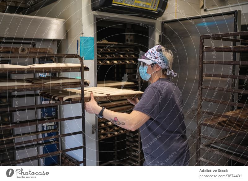 Frau bereitet Brot in der Bäckerei vor backen Ofen Koch Baguette Backblech Teigwaren roh Mundschutz Schutzschild neue Normale Coronavirus heiß Job Beruf Rezept