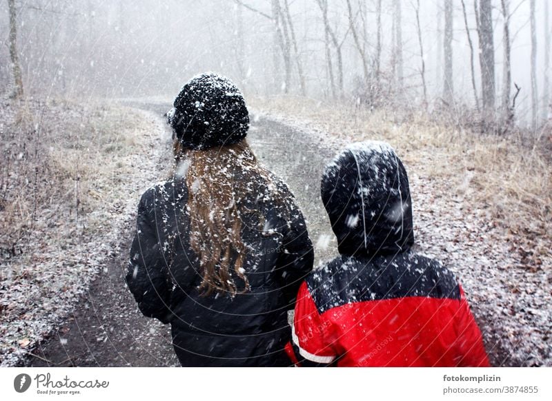 zwei Kinder auf einem Waldweg während es schneit Schneefall Schneeflocke Winter ein Kind sein Wintereinbruch zugeschneit Kindheit Schneeflocken Schneelandschaft
