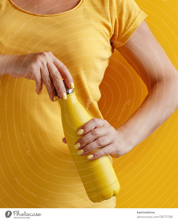 Nahaufnahme einer Frau, die eine gelbe wiederverwendbare Flasche auf gelbem Hintergrund hält Hand Monochrom ökologisch Wasser Stahl Thermo offen Halt hell