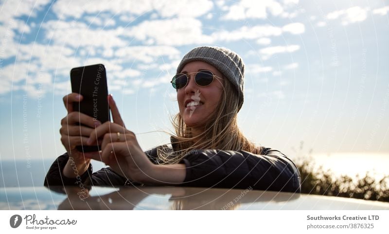 Junge Frau auf Autoreise Urlaub auf dem Dach eines Mietwagens gelehnt mit dem Handy fotografierend Junge Frauen Feiertag PKW fahren Fahrer Autovermietung Reisen