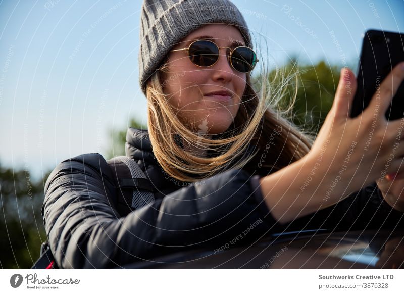 Junge Frau auf Autoreise Urlaub auf dem Dach eines Mietwagens gelehnt mit dem Handy soziale Netzwerke Junge Frauen Feiertag PKW fahren Fahrer Autovermietung