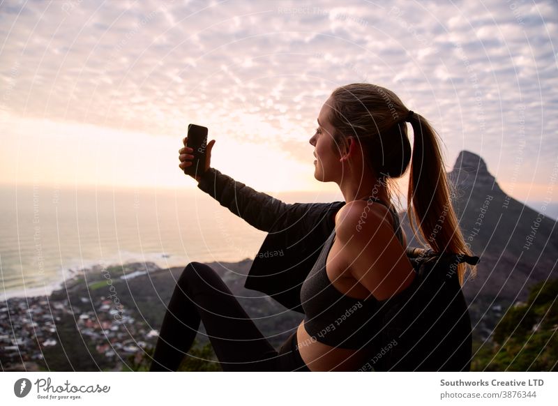Junge Frau mit Rucksack wandert entlang des Küstenpfades und posiert für Social Media Selfie auf dem Handy Sonnenuntergang Junge Frauen Wanderung wandern