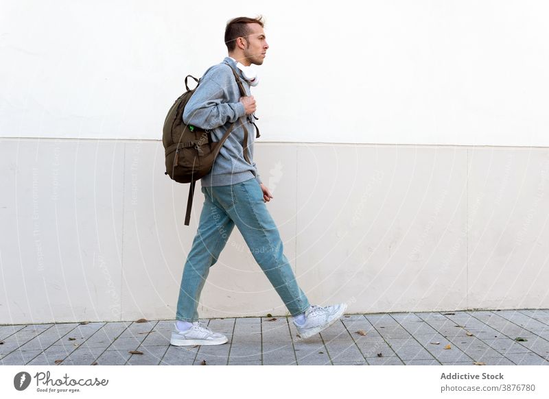 Junger Mann mit Rucksack zu Fuß in der Nähe der Wand Hipster lässig urban Spaziergang modern Stil trendy jung männlich Lifestyle Typ Fußgänger Reisender