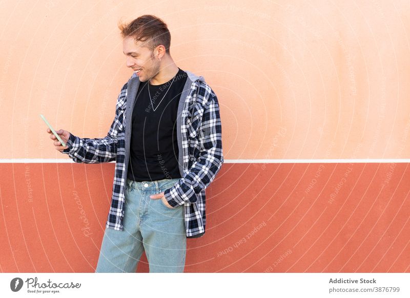 Fröhlicher Hipster-Mann mit Smartphone benutzend lässig heiter Nachricht Telefon modern Apparatur kariertes Hemd Mobile Inhalt jung männlich Gerät Browsen