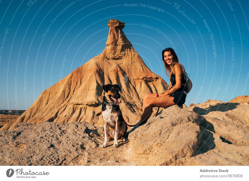 Lächelnde Frau mit Hund in felsiger Wüste wüst Urlaub Felsen reisen Zusammensein Abenteuer sonnig trocken bardenas reales Spanien Sommer Eckzahn sitzen Glück