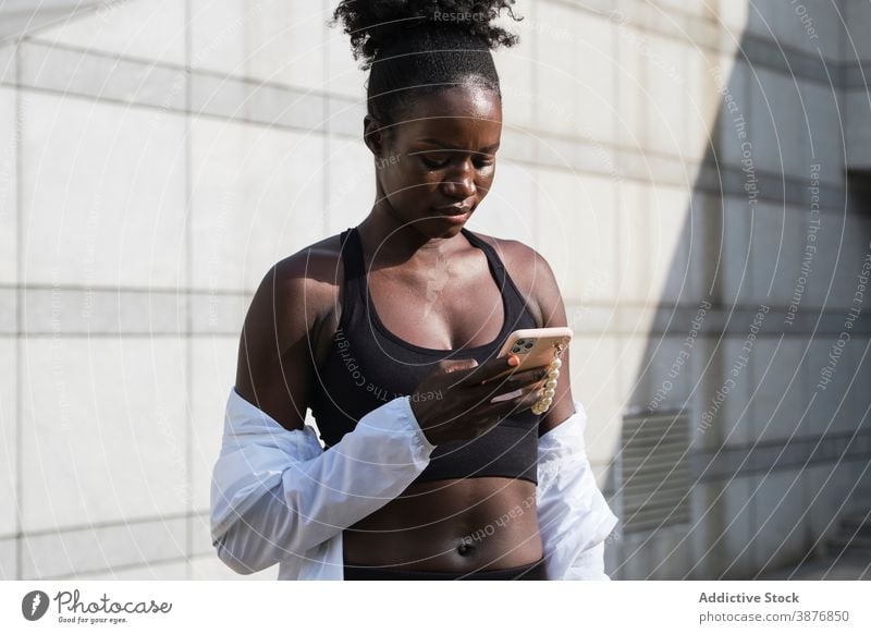 Schwarze Sportlerin beim Surfen auf dem Smartphone in der Stadt Training Pause Browsen Athlet Frau Nachricht Großstadt ethnisch schwarz Afroamerikaner Straße