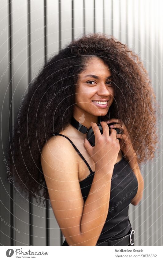 Erfreute schwarze Frau genießt Musik in Kopfhörern zuhören Straße genießen Gesang heiter krause Haare Afro-Look ethnisch Afroamerikaner Frisur positiv jung Wand