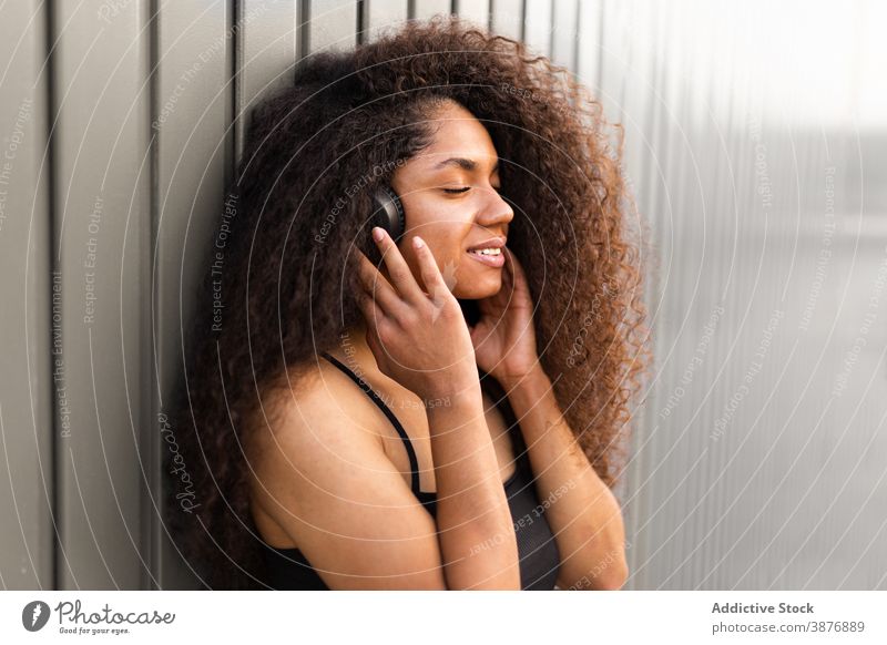 Charmante ethnische Frau mit Kopfhörer auf der Straße krause Haare Afro-Look Frisur charmant Lächeln natürlich Schönheit zuhören schwarz Afroamerikaner