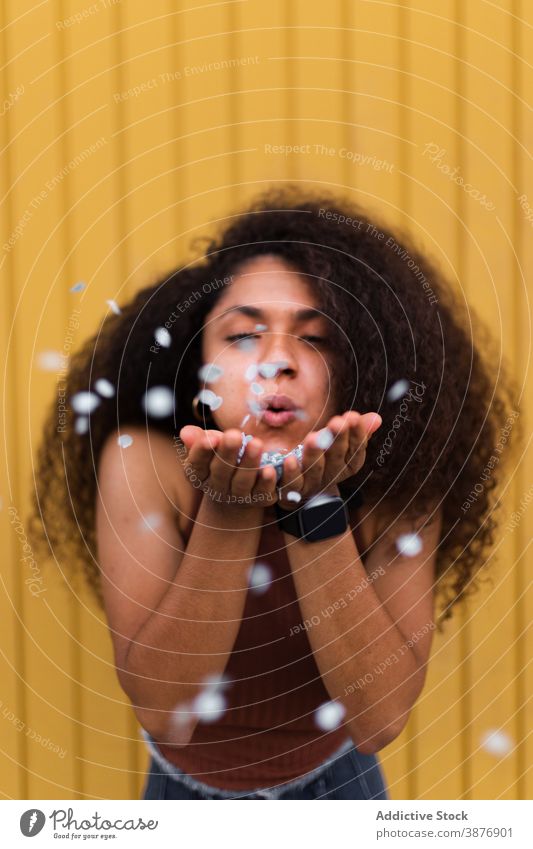 Schwarze Frau bläst Konfetti in Richtung Kamera Schlag festlich feiern Konzept Spaß haben Veranstaltung krause Haare Afro-Look ethnisch schwarz Afroamerikaner