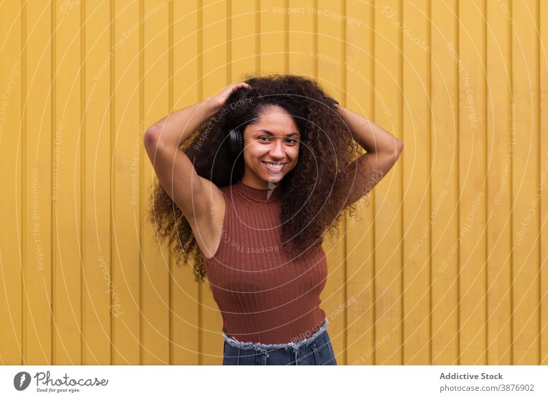 Charmante ethnische Frau mit Kopfhörer auf der Straße krause Haare Afro-Look Frisur charmant Lächeln natürlich Schönheit zuhören schwarz Afroamerikaner