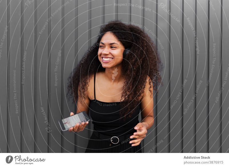 Optimistische schwarze Frau, die auf der Straße Musik hört zuhören Kopfhörer meloman genießen Afro-Look Frisur krause Haare Smartphone ethnisch Afroamerikaner