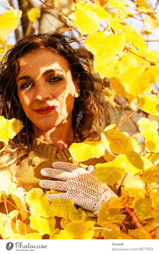 Frau unter gelbem Herbstlaub retuschieren Behaarung Blätter Park Garten Gelblich Lifestyle reif Porträt eine Person Baum Mantel gelber Überzieher Szene