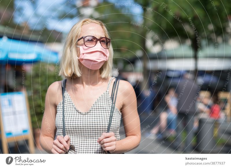 Porträt einer jungen Frau, die mit einer Schutzmaske zum Schutz vor dem Covid-19-Virus auf der Straße geht. Beiläufige Personen im Hintergrund Mundschutz