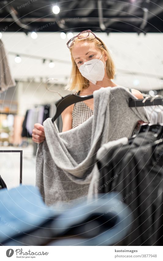 Modische Frau mit Gesichtsschutzmaske trägt Einkaufskleidung im wiedereröffneten Einzelhandelsgeschäft. Neuer normaler Lebensstil während einer Coronavirus-Pandemie