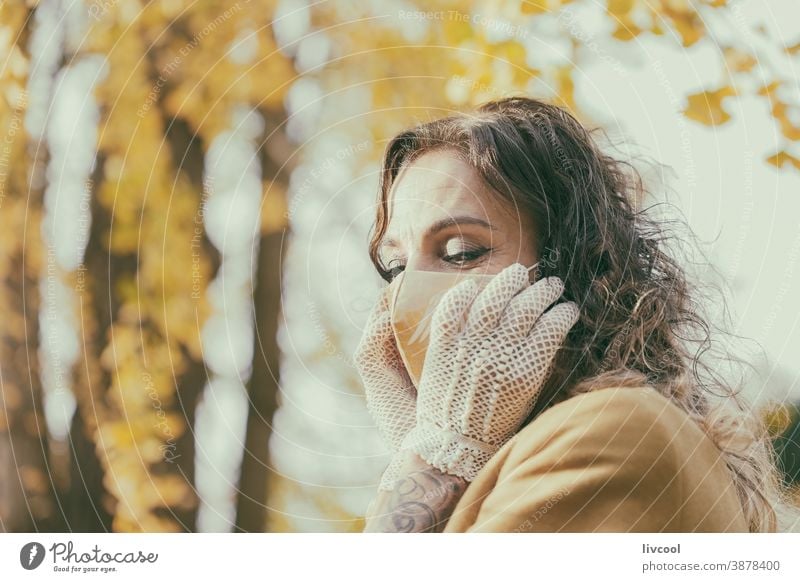 Frau mit Handschuhen, die ihre Maske berühren berührend Mundschutz gelb Park Garten Gelblich Blätter Lifestyle reif Porträt eine Person Baum Mantel