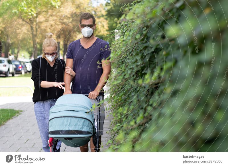 Besorgter junger Elternteil, der auf einer leeren Straße mit einem Kinderwagen unterwegs ist und medizinische Masken trägt, die ihn vor dem Coronavirus schützen sollen. Sozial distanziertes Leben während einer Coronavirus-Pandemie