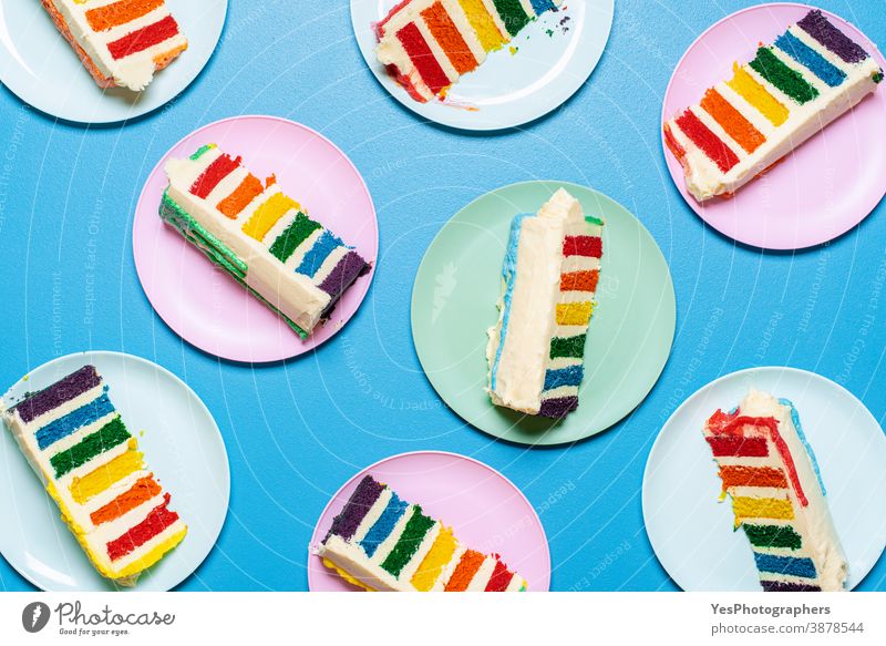 Regenbogenkuchenscheiben auf bunten Tellern auf blauem Tisch. Draufsicht auf Schichtkuchen mit Buttercreme lgbt obere Ansicht Geburtstagstorte