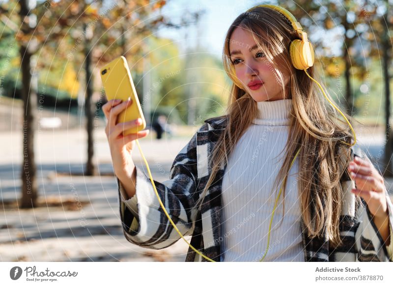 Trendy junge Frau mit gelben Kopfhörer und Smartphone im Herbst Park Selfie benutzend farbenfroh trendy Stil tausendjährig kariert Musik zuhören Farbe Drahtlos