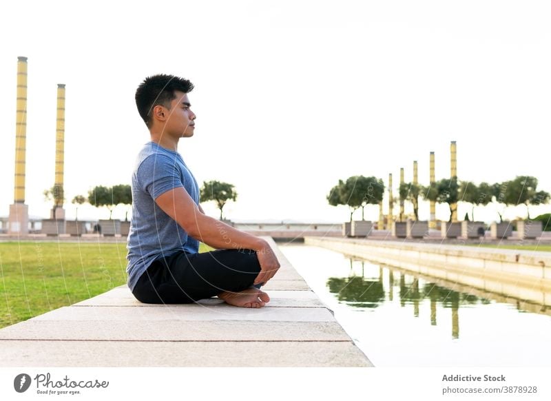 Gelassener Mann in Lotus-Pose im Park vermittelnd meditieren Yoga Harmonie Asana padmasana beweglich Beine gekreuzt üben männlich ethnisch asiatisch Unterlage