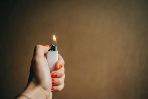 Eine weibliche Hand hält ein brennendes Feuerzeug anzünden zündend Licht Flamme heiß Nagellack entzünden zündeln Frauenhand Zünden Hintergrund neutral Wärme